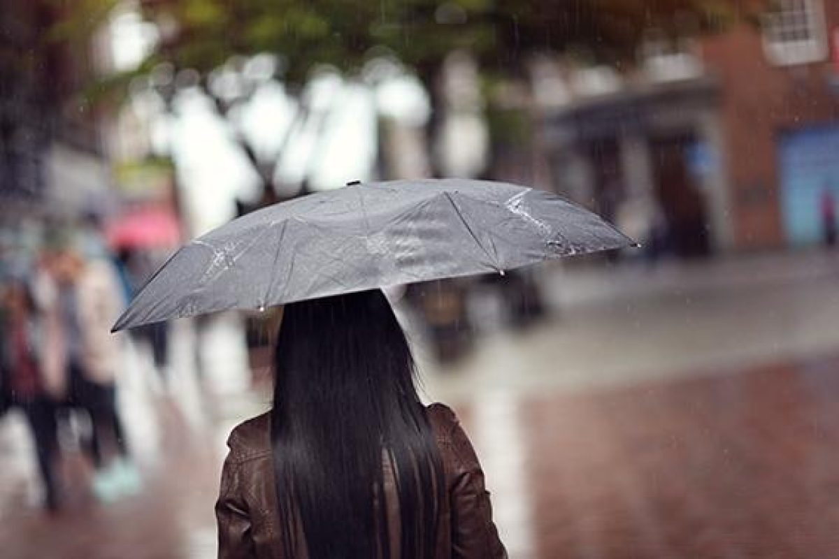 Rain drops falling on a woman holding a black umbrella in a shopping street scene concept for bad weather, winter or protection